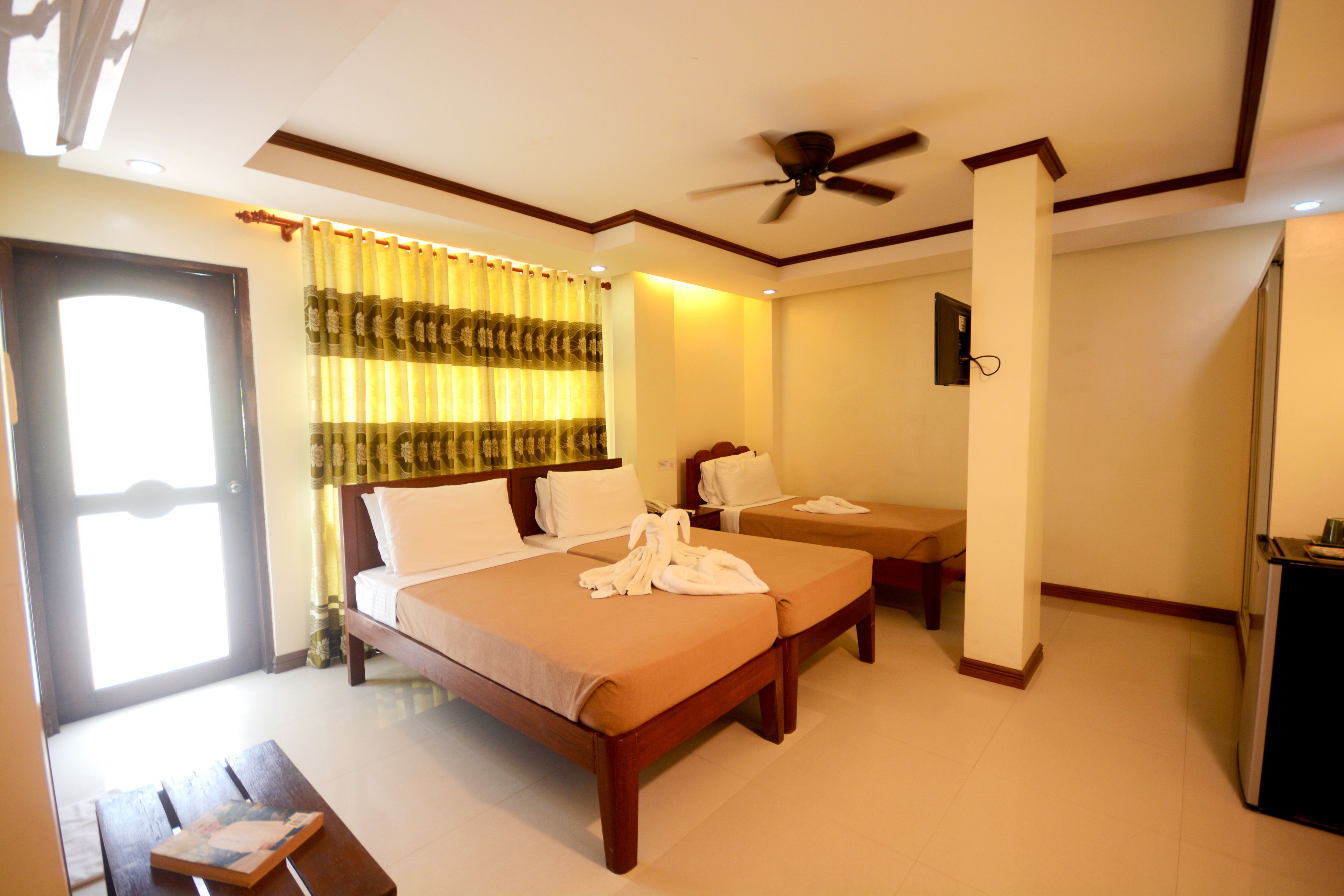 A hotel room with a large bed, a smaller bed, a desk, and a ceiling fan.