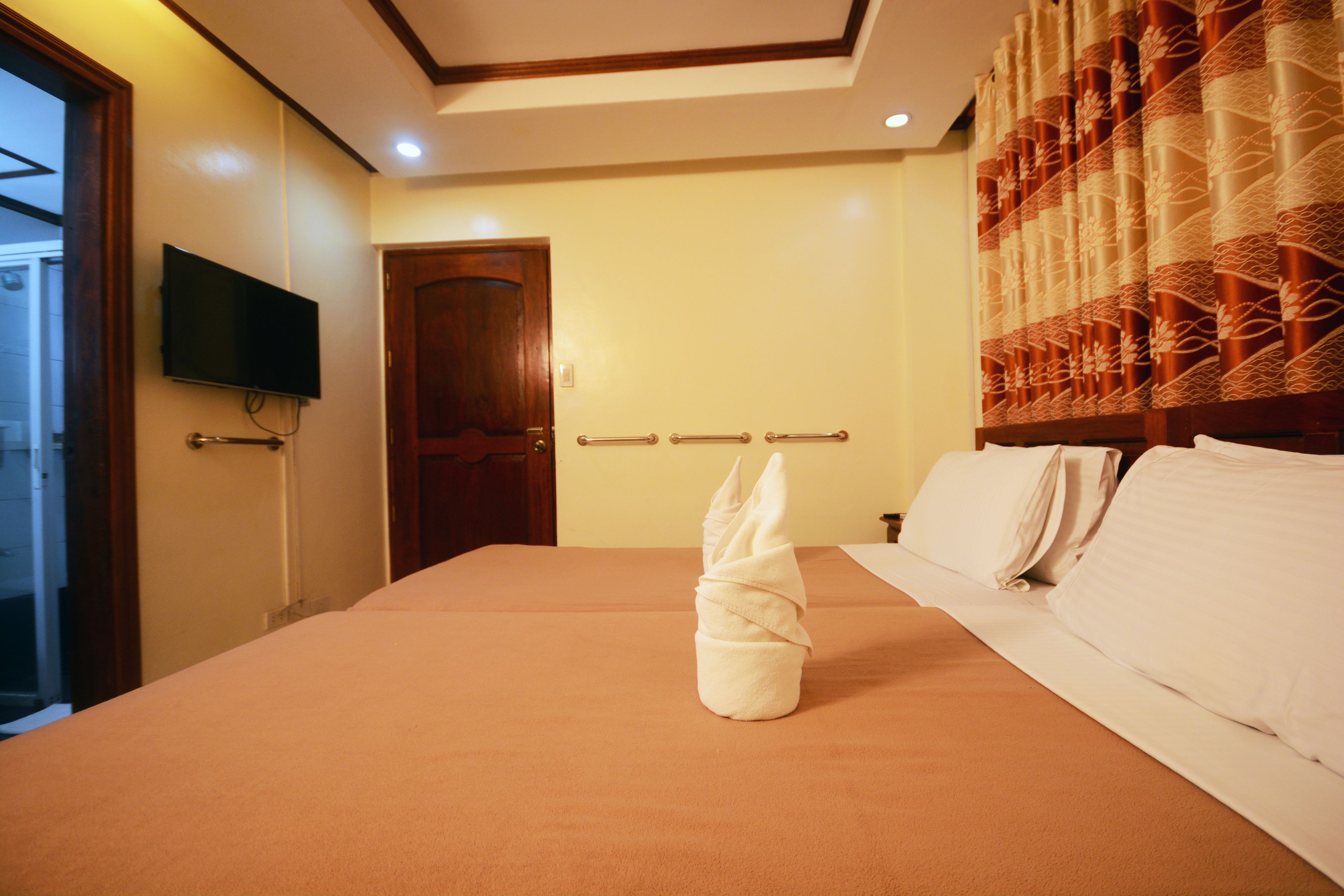 A hotel room with a large bed, a flat-screen TV mounted on the wall, and a wooden door.