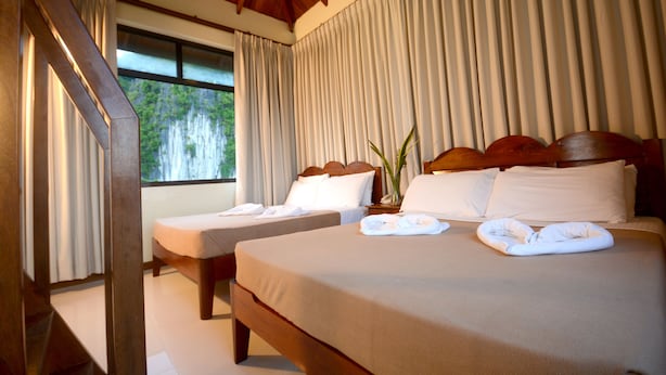 Habitación de hotel con dos camas, cabeceros de madera y un ventanal con cortinas.