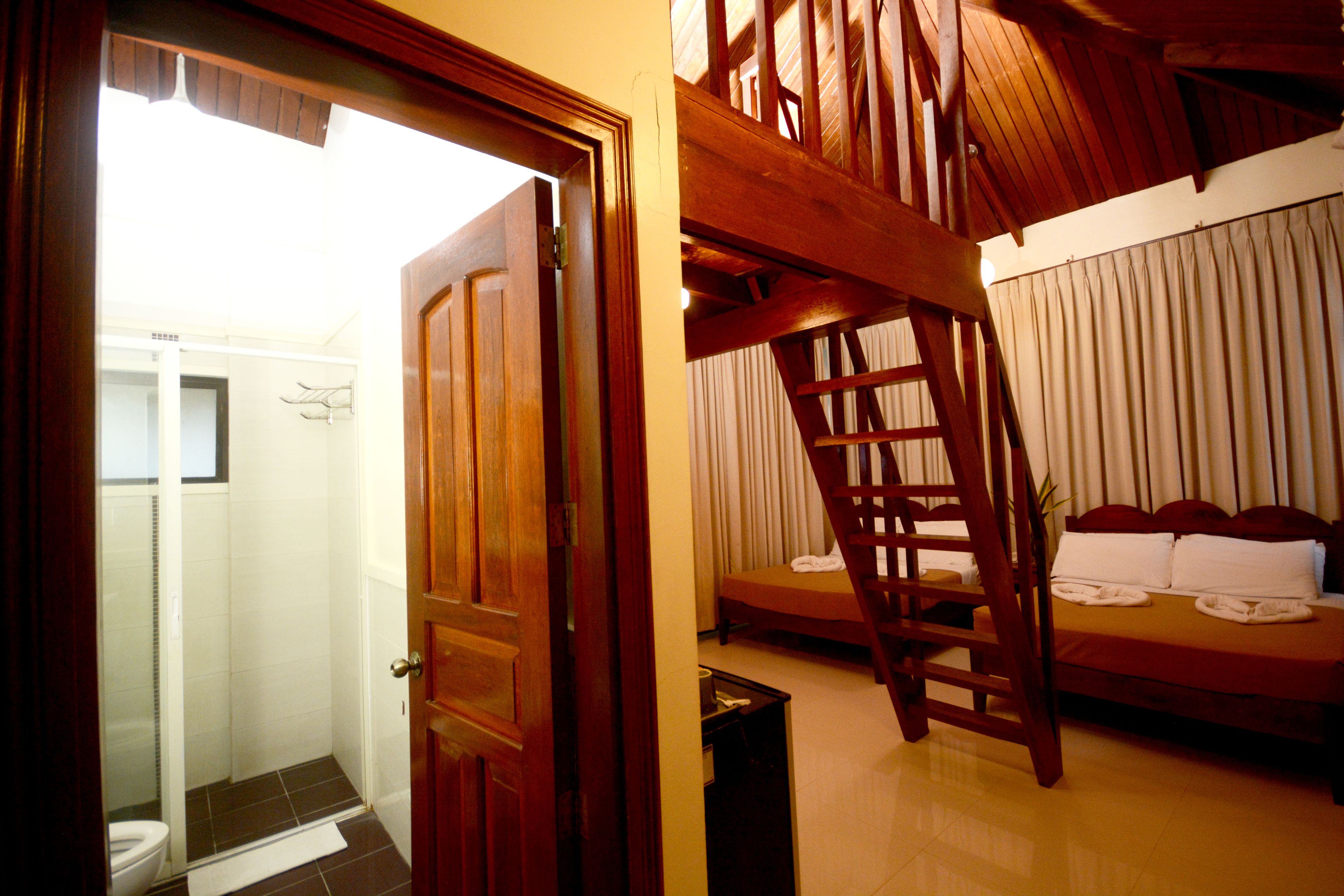 Ein Hotelzimmer mit einer Holztreppe, einem Bett mit weißer Bettwäsche und einem Badezimmer mit Toilette und Dusche.