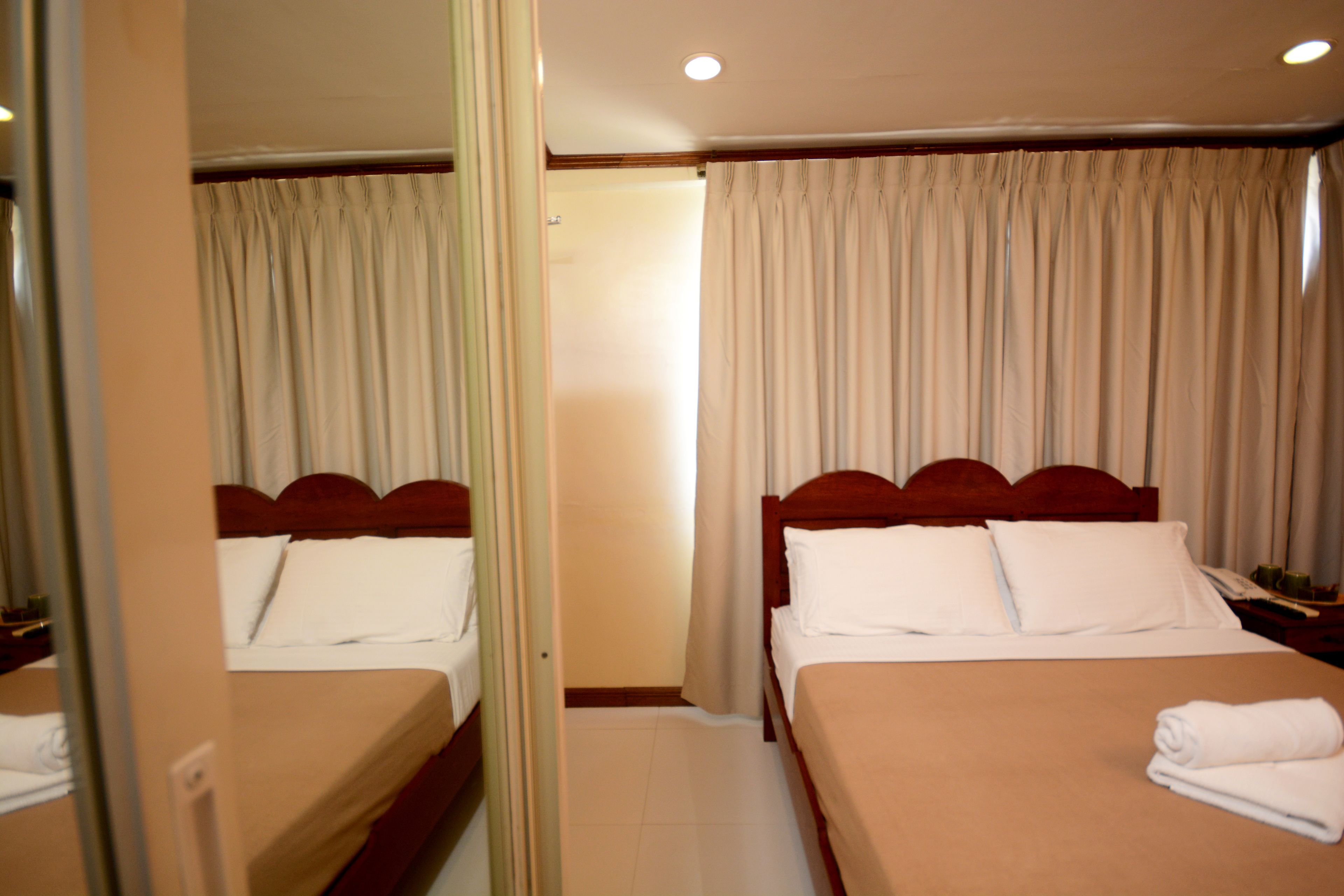 A hotel room with two beds, a mirror, a wooden headboard, and a curtain.