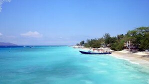 A beach with clear turquoise waters, a boat, and a small structure with umbrellas.