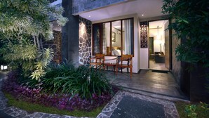 A modern building with a stone facade, a balcony with a patterned railing, and a well-lit entrance area with a seating arrangement.