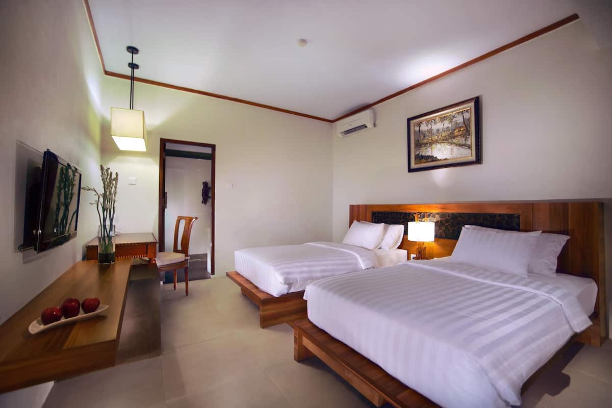 Une chambre d’hôtel avec deux lits, un bureau en bois sur lequel se trouve une assiette de pommes, une chaise, un téléviseur et un tableau accroché au mur.