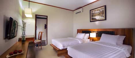 Habitación de hotel con dos camas, un escritorio de madera con un plato de manzanas, una silla, un televisor y un cuadro en la pared.