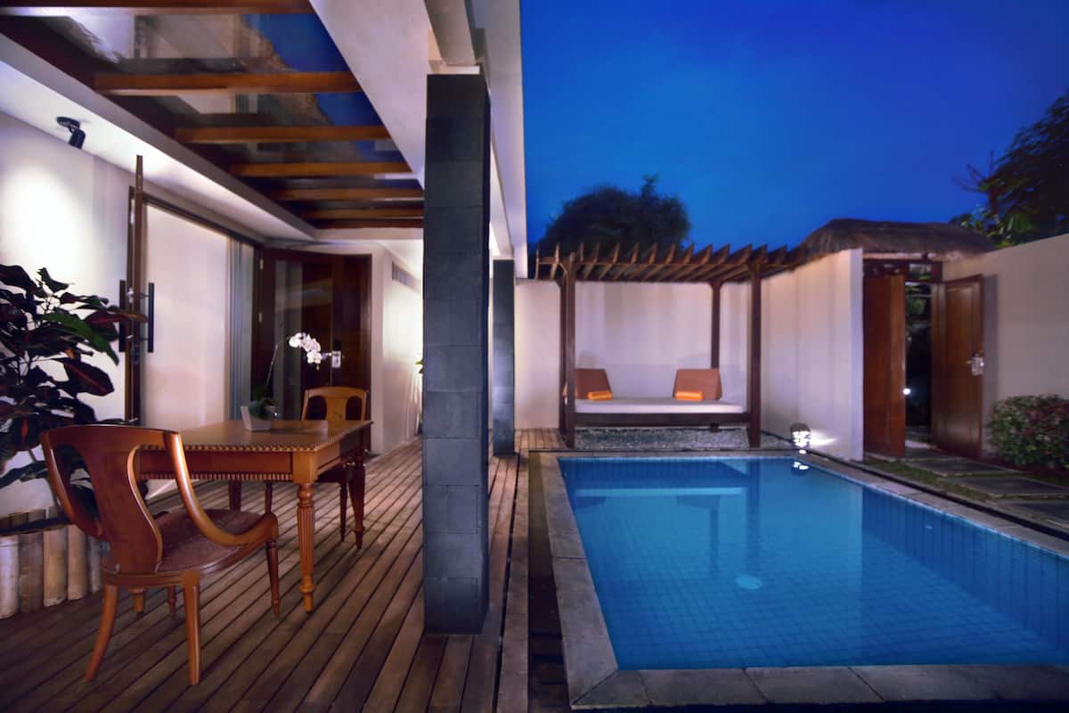 Une terrasse en bois avec une piscine, un coin repas avec des chaises et un espace détente avec des coussins.