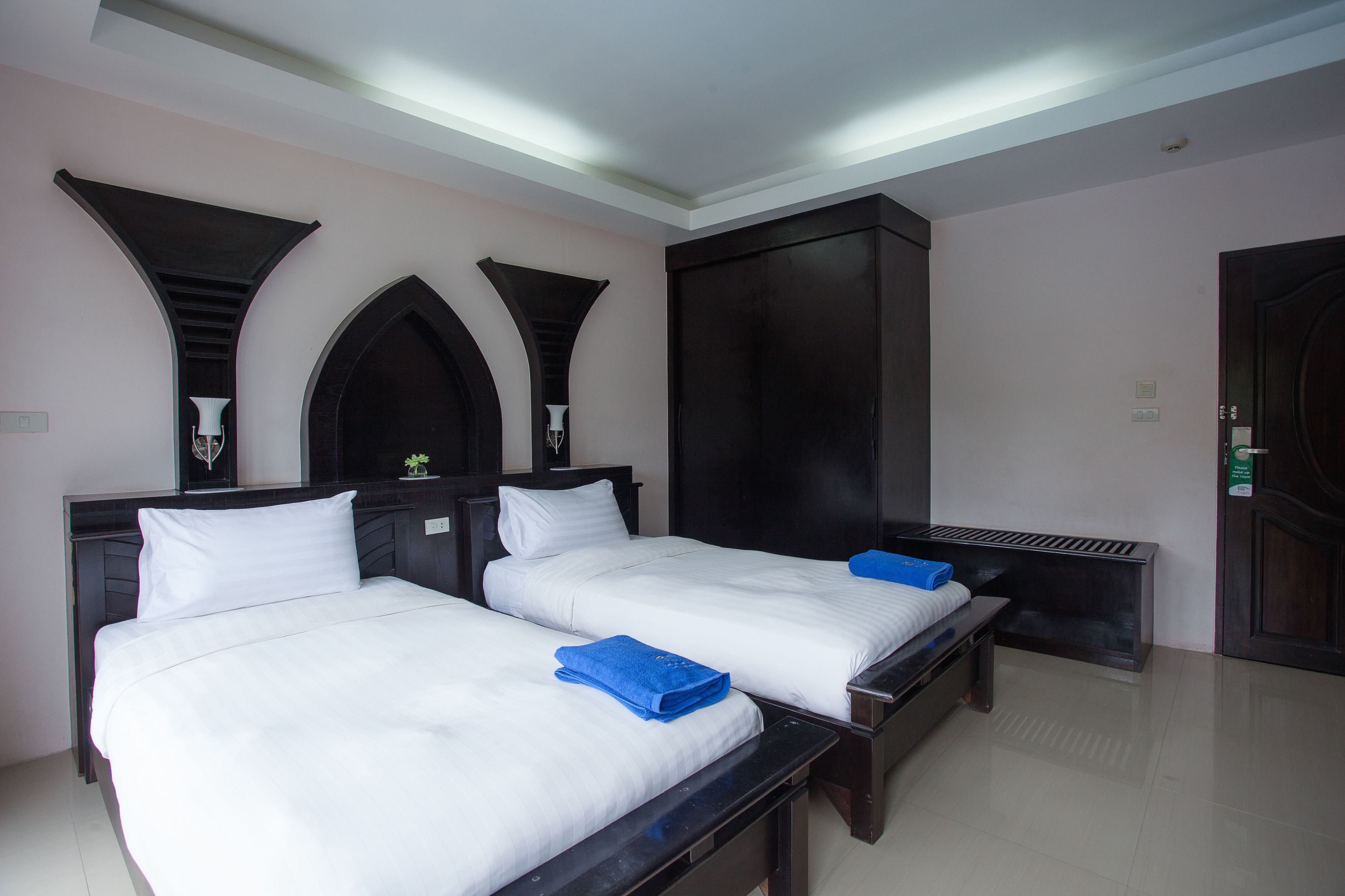 Quarto de hotel com duas camas, um guarda-roupa e um banquinho.