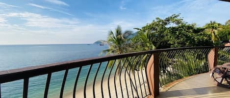 Un balcón con vistas al mar, palmeras y una isla distante.