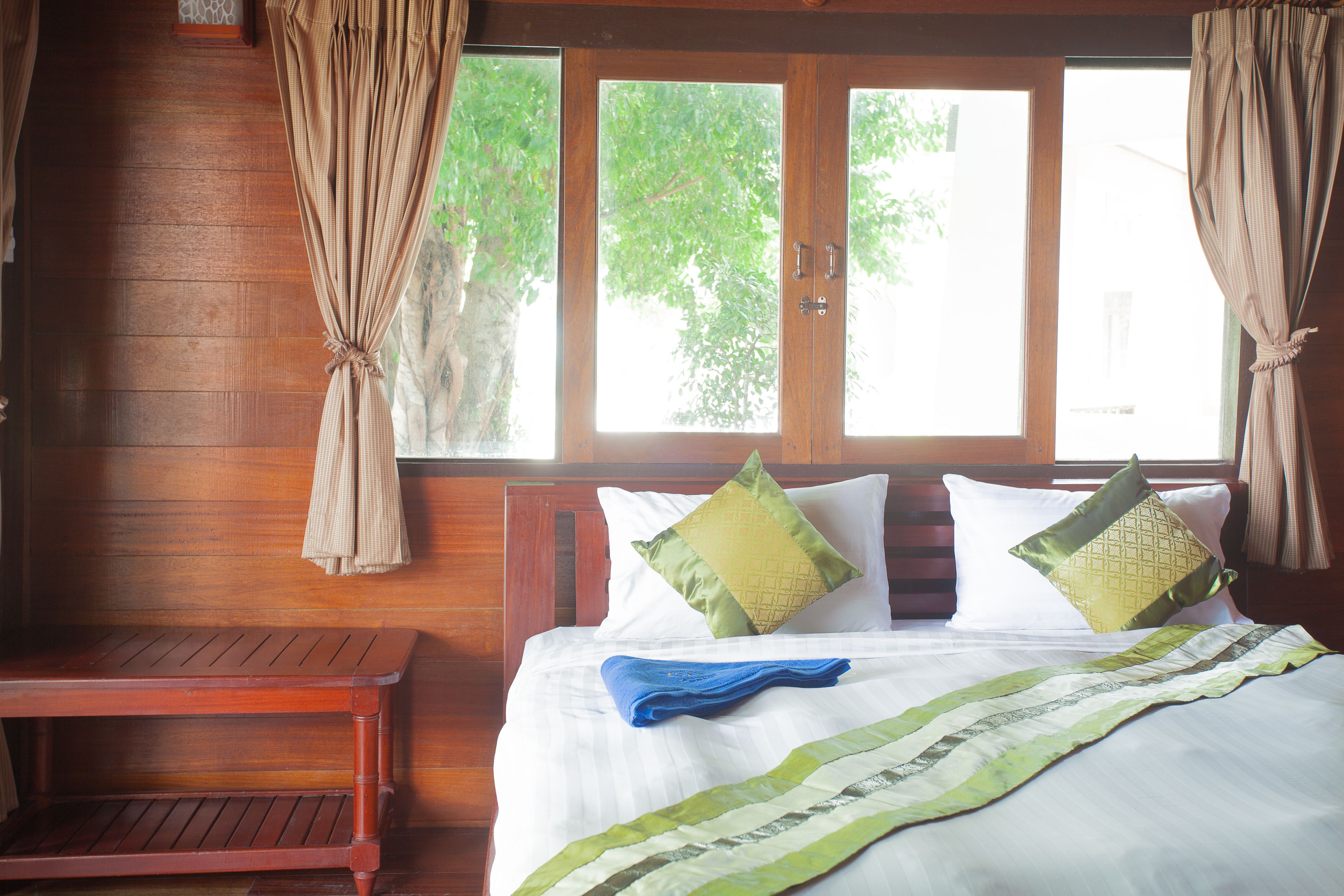 A wooden room with a bed, two pillows, a blue towel, and a bench.