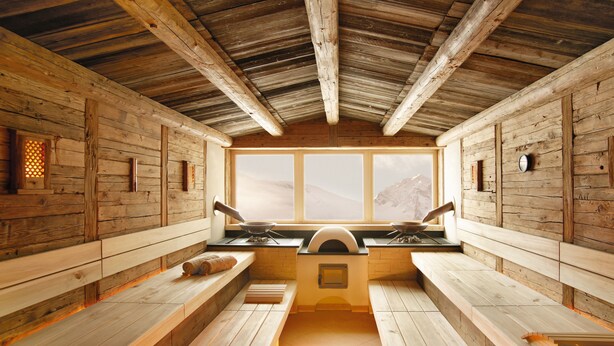 A rustic wooden cabin with a central cooking area, benches, and a large window overlooking a mountainous landscape. - Hotel Alpenhof (Tux)