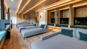 A modern spa with multiple seating areas, wooden beams, and a fireplace. - Hotel Alpenhof (Tux)