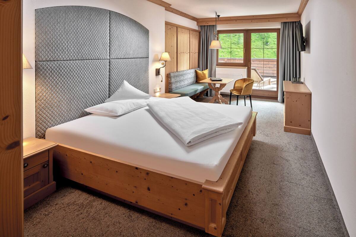 Habitación de hotel con una cama de madera, un sofá, un escritorio y vistas al exterior.