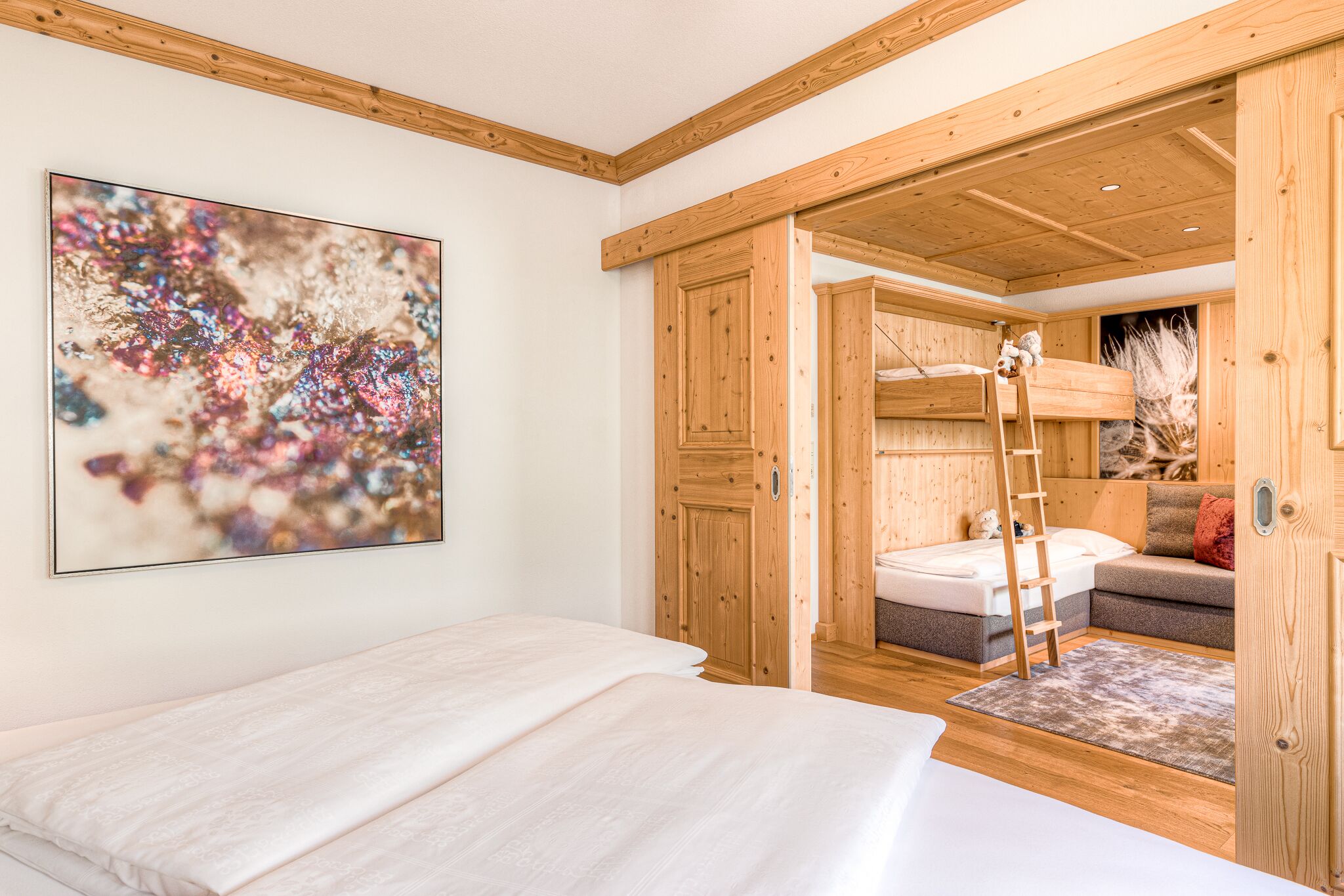 A bedroom with a bed, a wooden ladder, a sofa, and a painting on the wall.