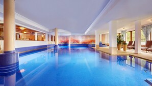 An indoor swimming pool with clear blue water, surrounded by lounge chairs and a mural on the wall. - Hotel Alpenhof (Tux)