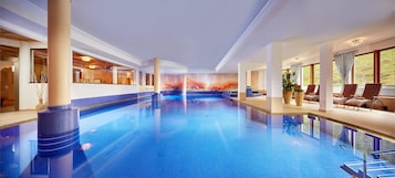Una piscina interior con agua cristalina, rodeada de sillones de descanso y un mural en la pared.