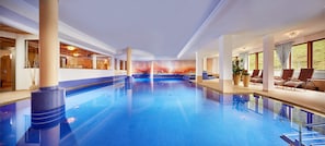 An indoor swimming pool with clear blue water, surrounded by lounge chairs and a mural on the wall.