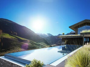 Una piscina infinita moderna con vista a la montaña, arquitectura de madera y cielo despejado.