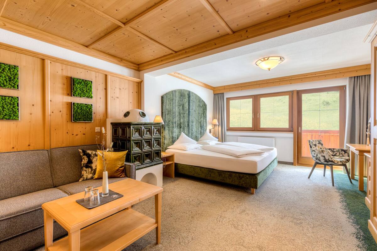 Habitación de hotel con techo de madera, cama, sofá, mesa y vistas al exterior.