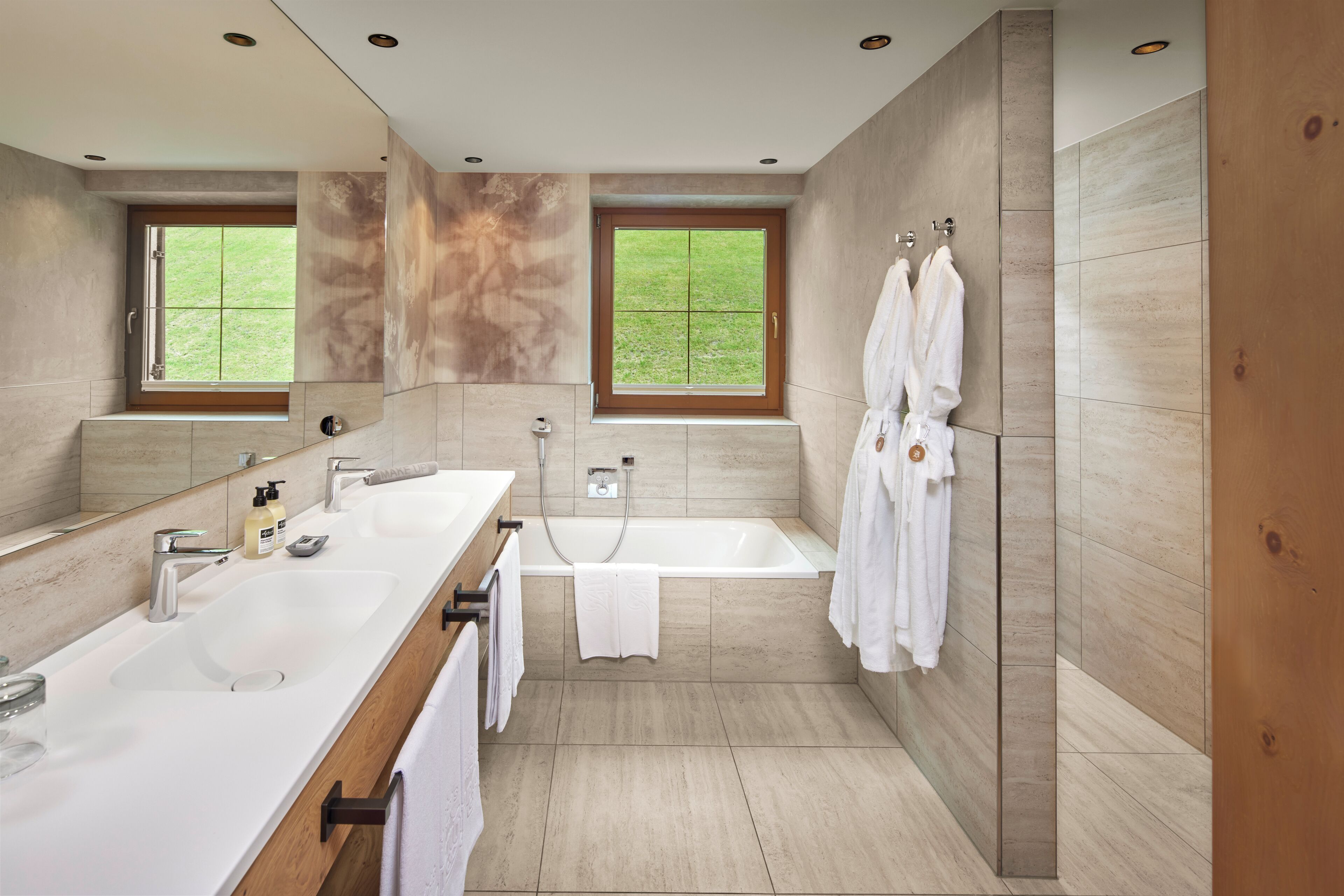 A modern bathroom with two sinks, a bathtub, and large windows.