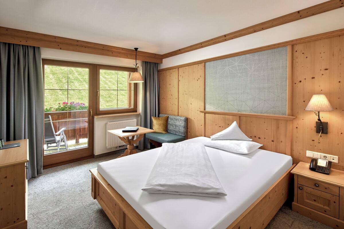 Un dormitorio con paneles de madera, una cama grande, un escritorio y vistas al exterior con vegetación.