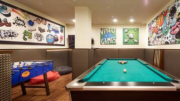 A pool table with a green felt surface, a foosball table, and various wall art including a 'Video Games' sign.