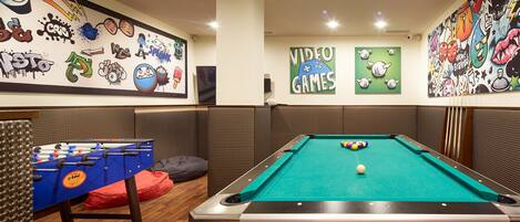 A pool table with a green felt surface, a foosball table, and various wall art including a 'Video Games' sign.