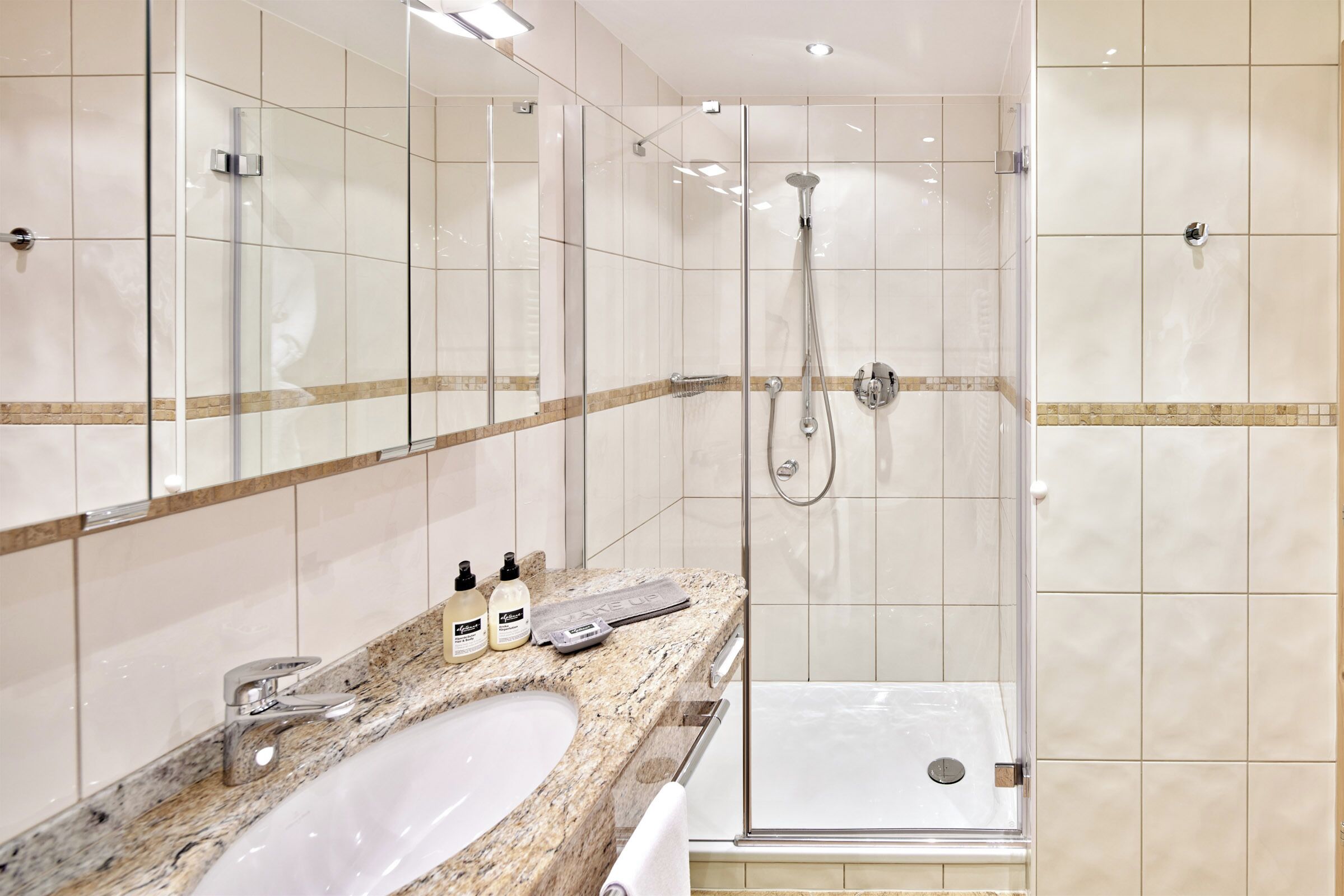 Un baño moderno con encimera de granito, cabina de ducha con paredes de vidrio y un espejo grande.