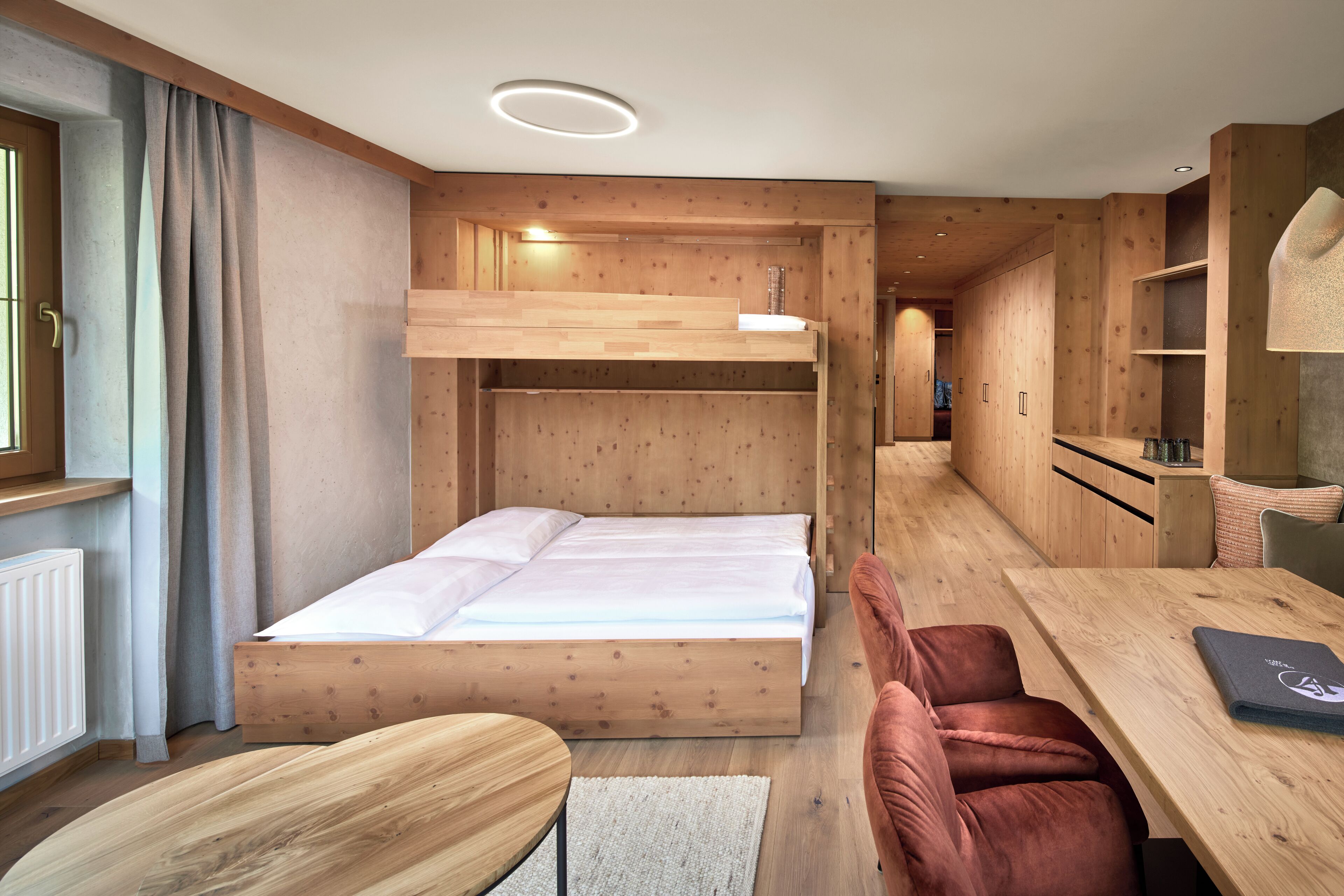 Una habitación moderna con una litera, muebles de madera, una mesa de comedor y una zona de cocina integrada.