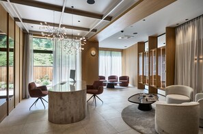 A modern interior with a round glass table, red chairs, a round coffee table, and a unique ceiling light fixture. - Hotel Alpenhof (Tux)