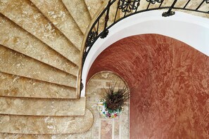 A spiral staircase with a metal railing, leading to an arched doorway with a potted plant.