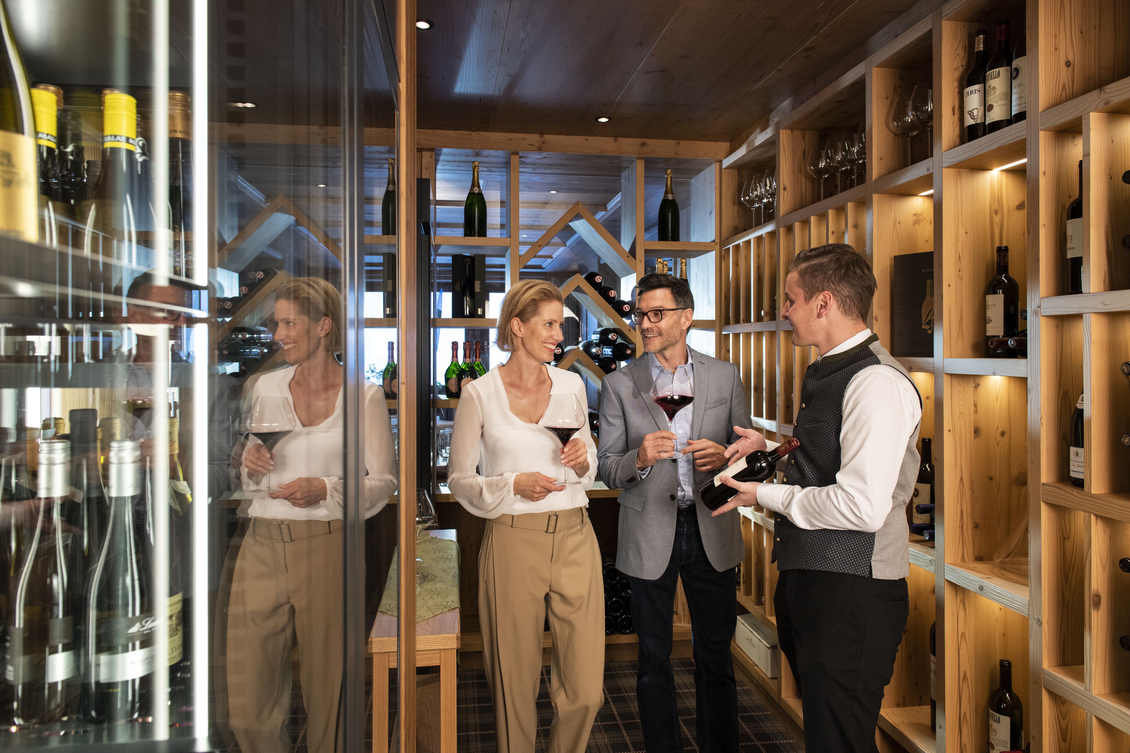 A wine cellar with wooden shelves and glass cases containing wine bottles.
