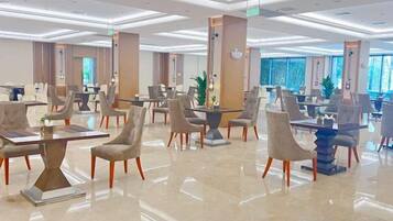 A spacious hotel lobby with multiple seating areas, including tables and chairs, and a large plant in the center.