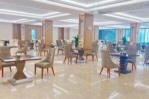 A spacious hotel lobby with multiple seating areas, including tables and chairs, and a large plant in the center. - Sun Plaza International Hotel (Jining)