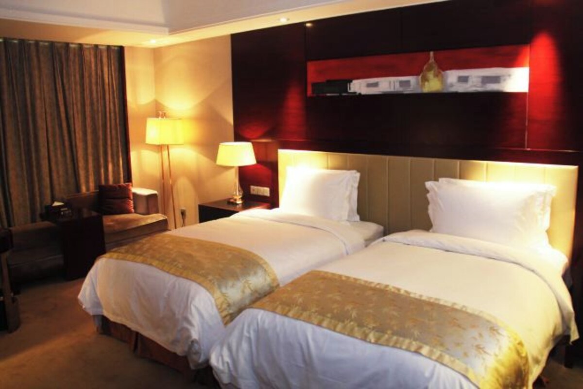 A hotel room with two beds, a desk, a chair, and a lamp.