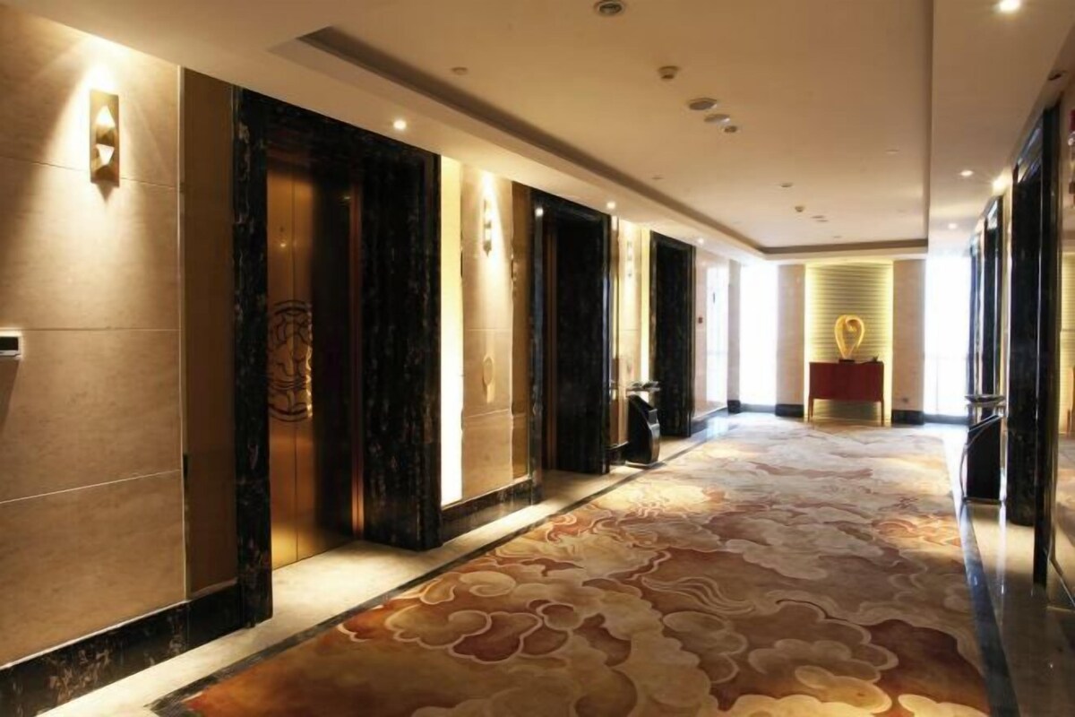 A hotel corridor with marble walls, a patterned carpet, and a reception desk in the distance.