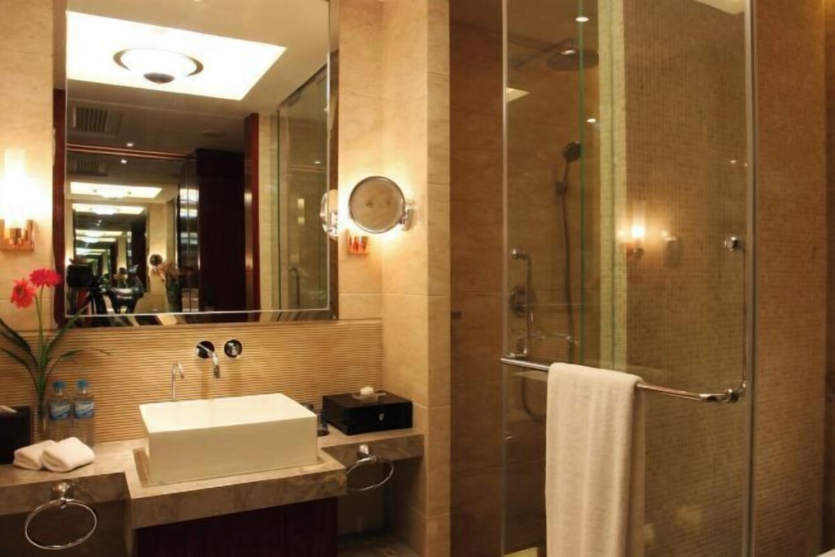 A modern bathroom with a large mirror, a rectangular sink, a glass shower enclosure, and a towel rack.