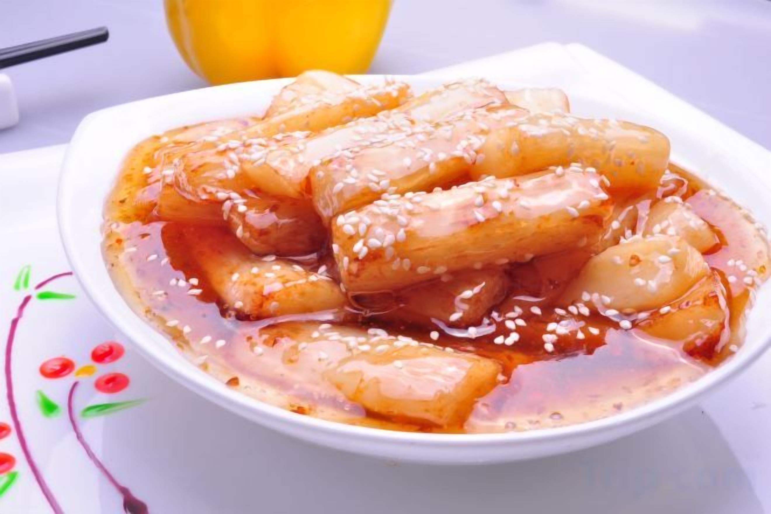 A bowl of food with a glossy sauce and sesame seeds.