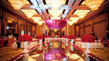 A banquet hall with a long table, chandeliers, and red floral arrangements.