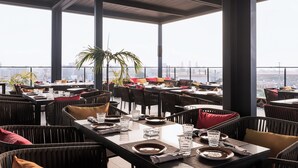 A rooftop restaurant with tables set for dining, large windows, and a view of the city skyline. - Riviera Royal Hotel (Conakry)