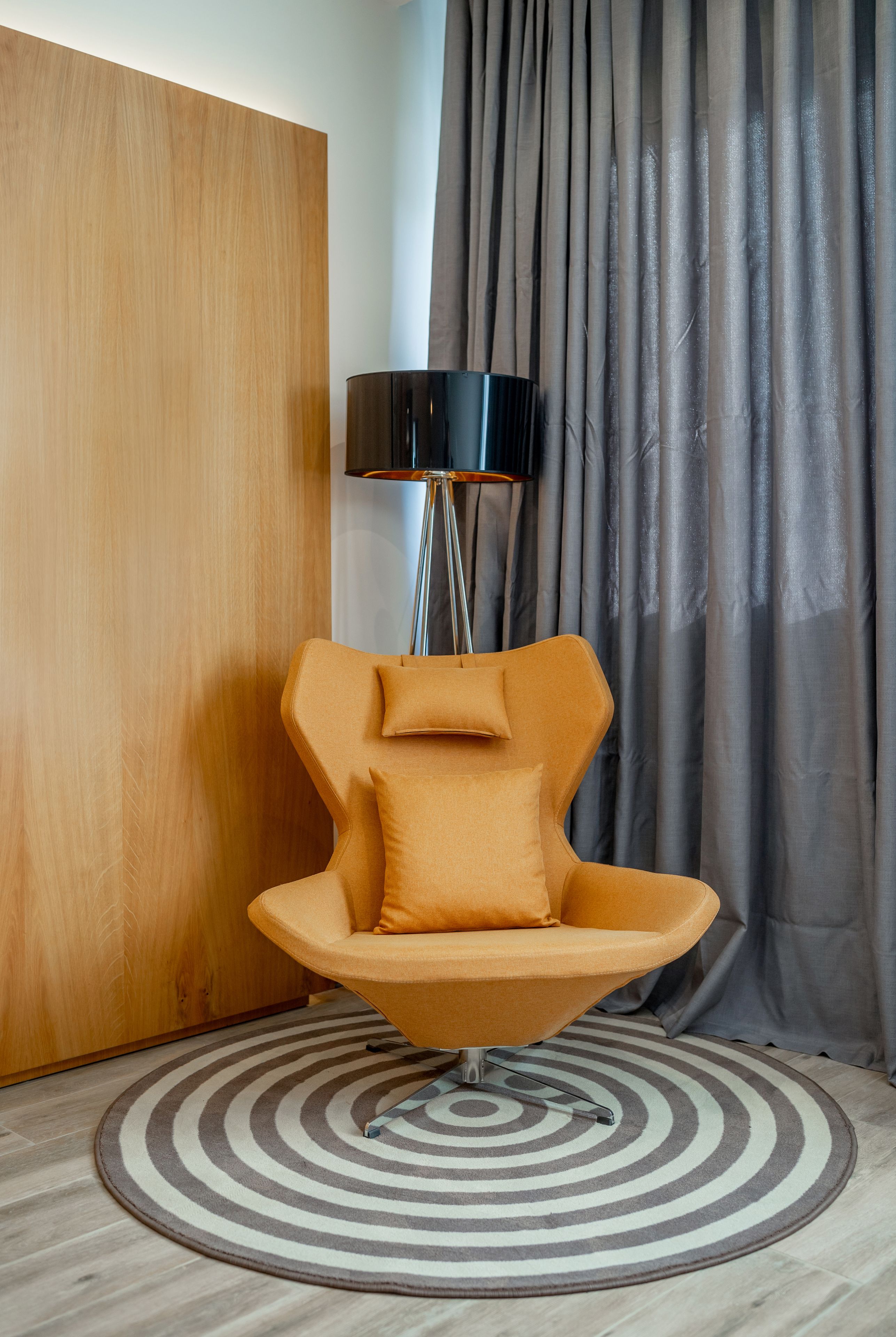 Una habitación moderna con un panel de pared de madera, un tapete redondo y una silla naranja original, además de una lámpara de pie.