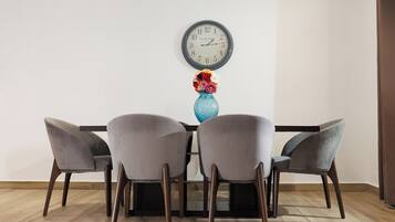 Un comedor con una mesa, cuatro sillas, un jarrón con flores y un reloj de pared.