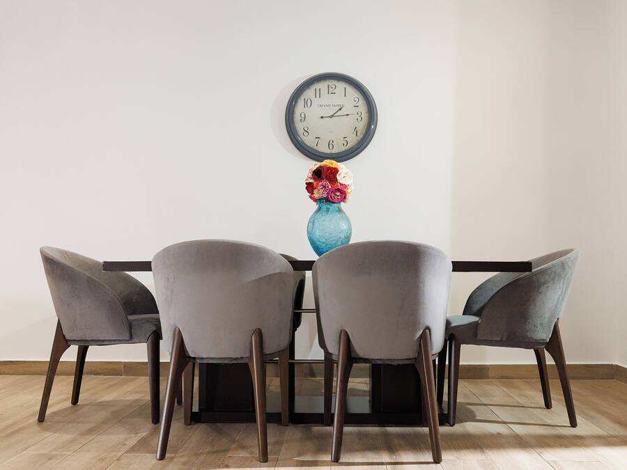 Un comedor con una mesa, cuatro sillas, un jarrón con flores y un reloj de pared.