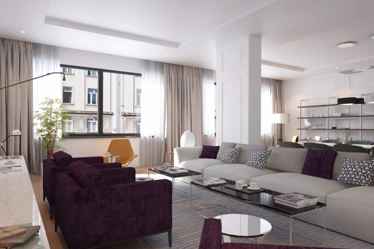 Ett modernt vardagsrum med en soffa, fåtöljer och ett soffbord. Det finns ett stort fönster med gardiner, en växt och en bokhylla.