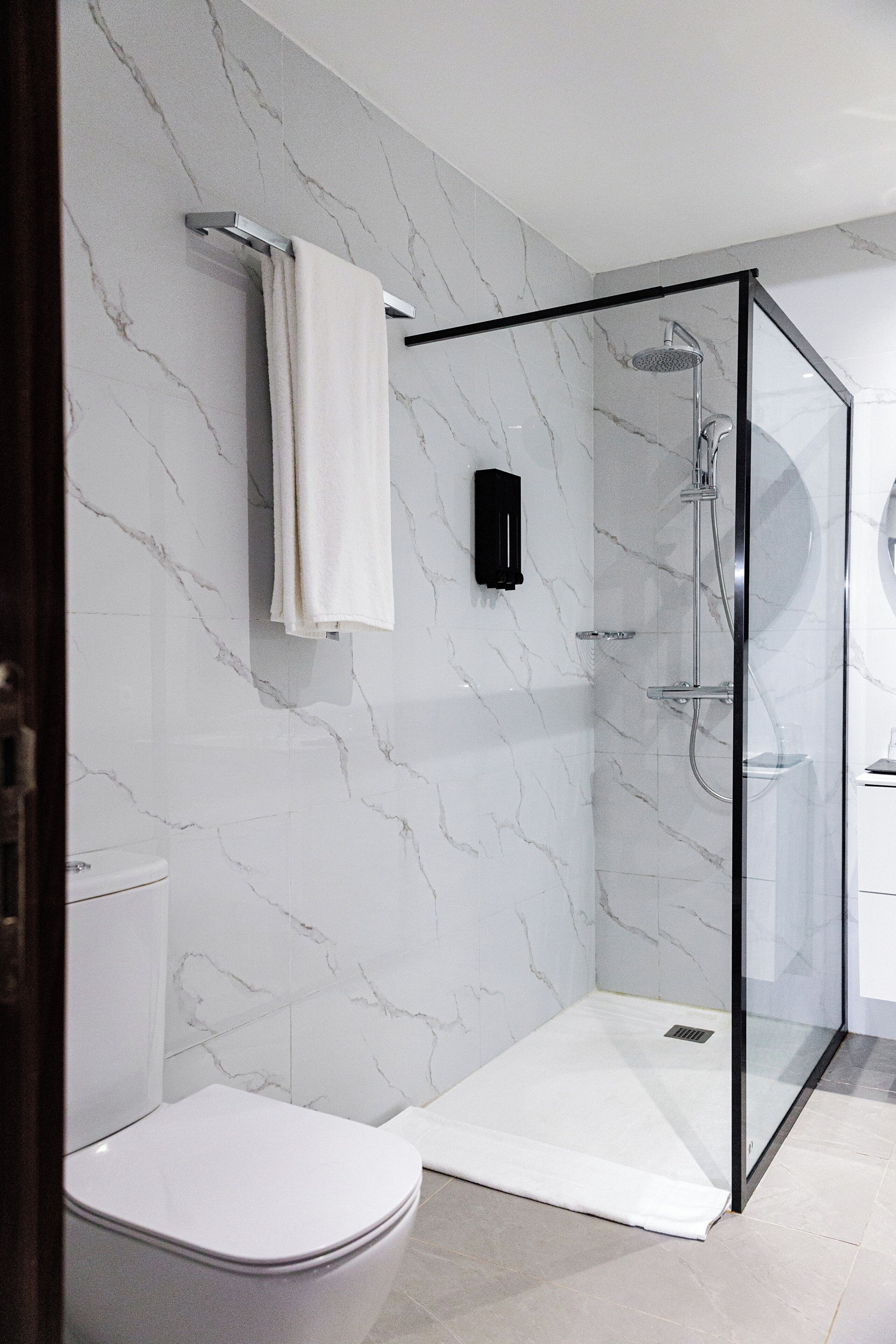 Une salle de bain moderne avec une douche à parois de verre, des toilettes blanches et un mur en marbre.