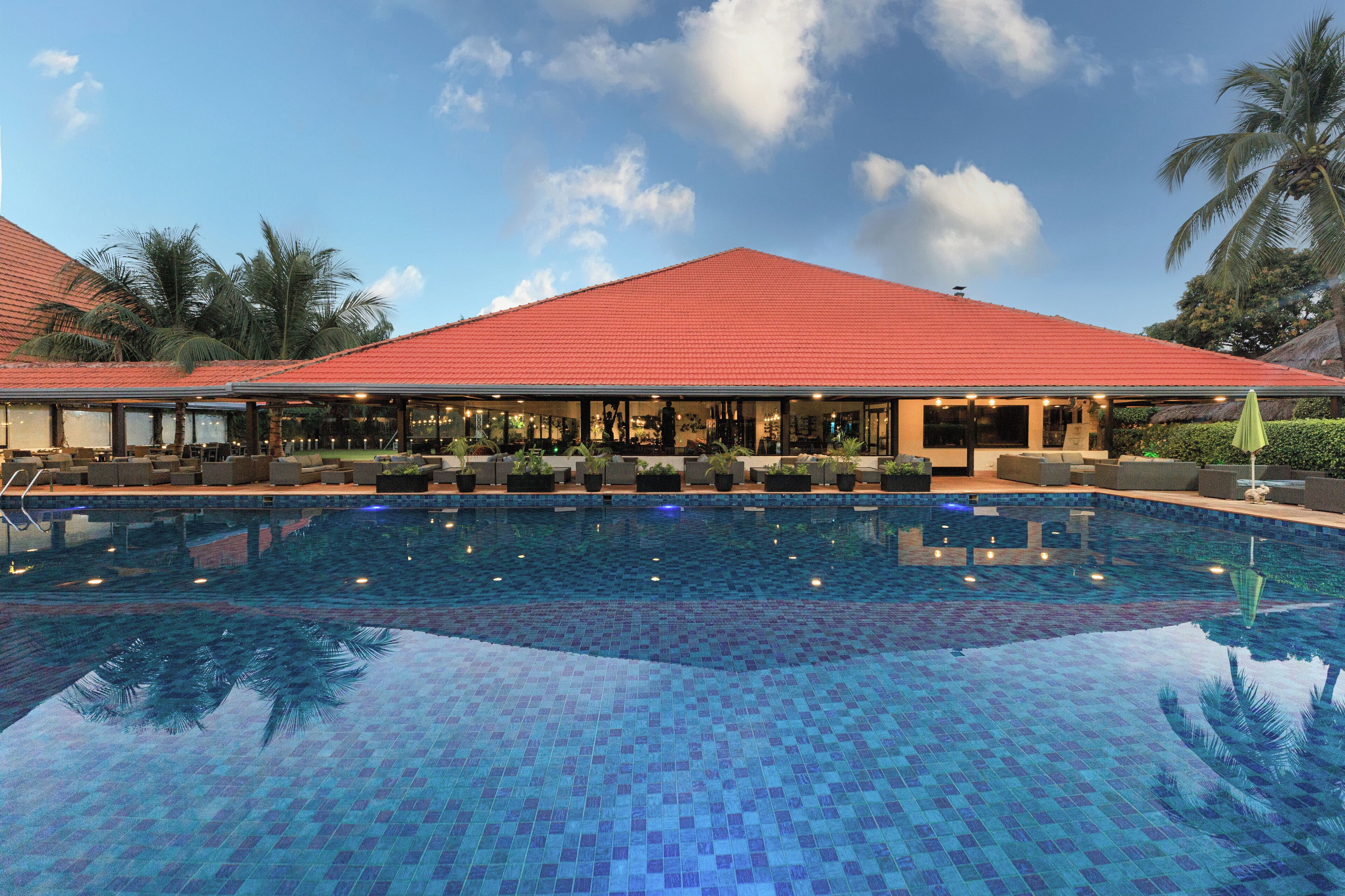 A swimming pool with a tiled floor and a building with a red roof in the background.