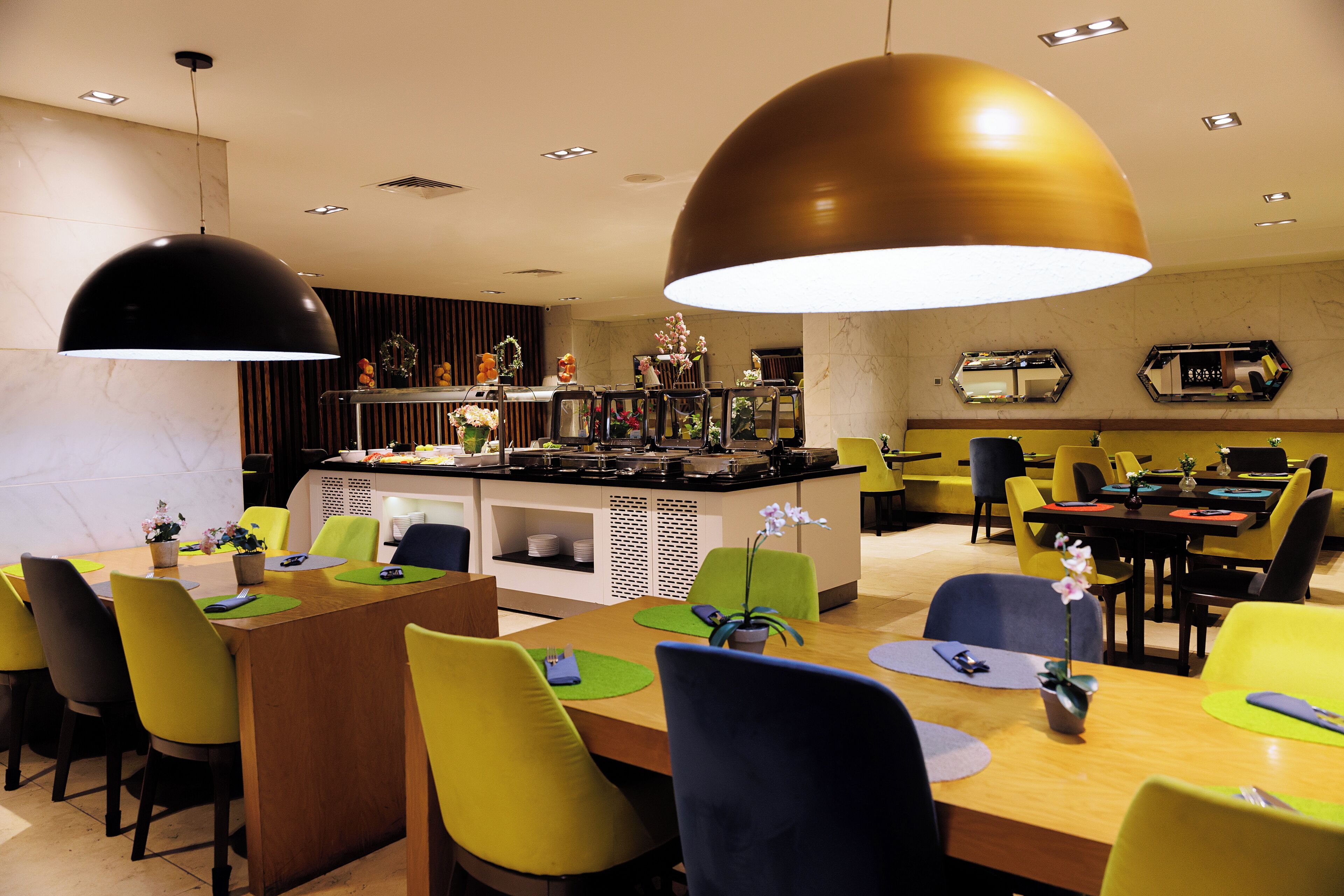 Un comedor moderno con sillas amarillas y azules, una isla central con cocina e iluminación colgante.