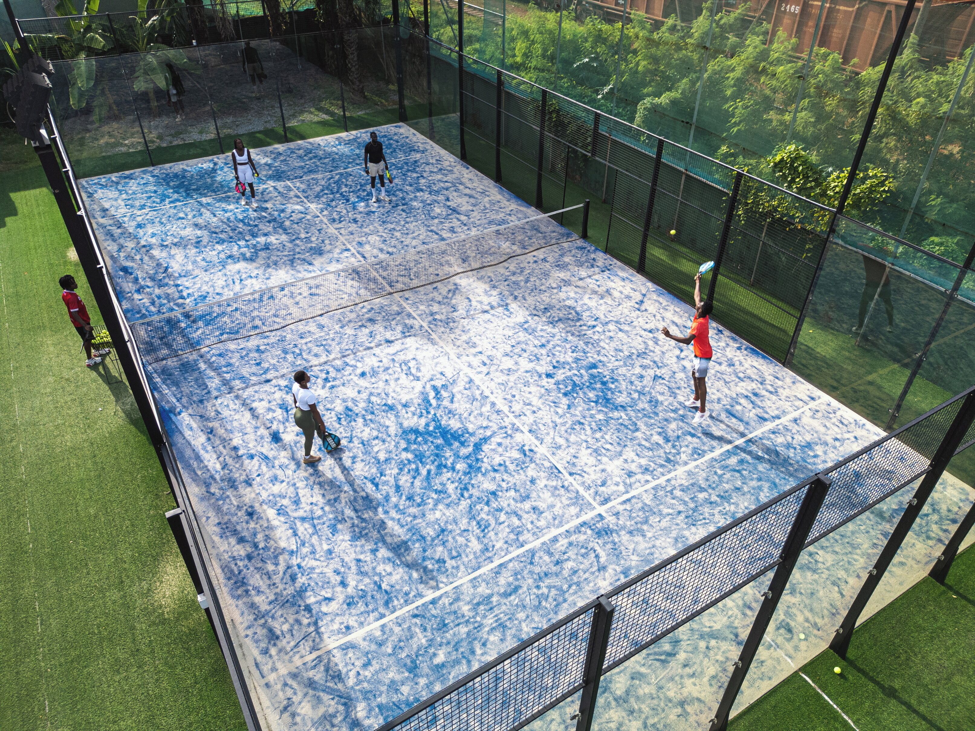 An indoor tennis court with a net, surrounded by a fence and greenery.