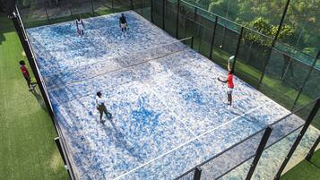 An indoor tennis court with a net, surrounded by a fence and greenery.