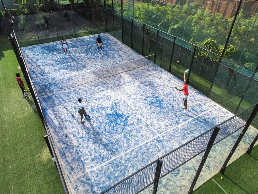 An indoor tennis court with a net, surrounded by a fence and greenery.