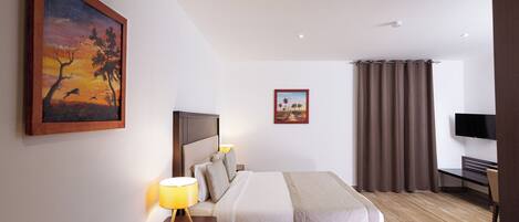 Una habitación de hotel con cama, mesitas de noche, televisor y obras de arte en las paredes.